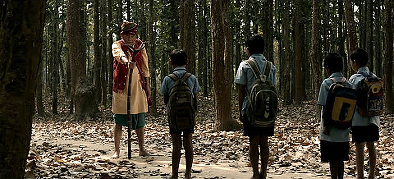 Film still: schoolchildren facing a figure on a forest path
