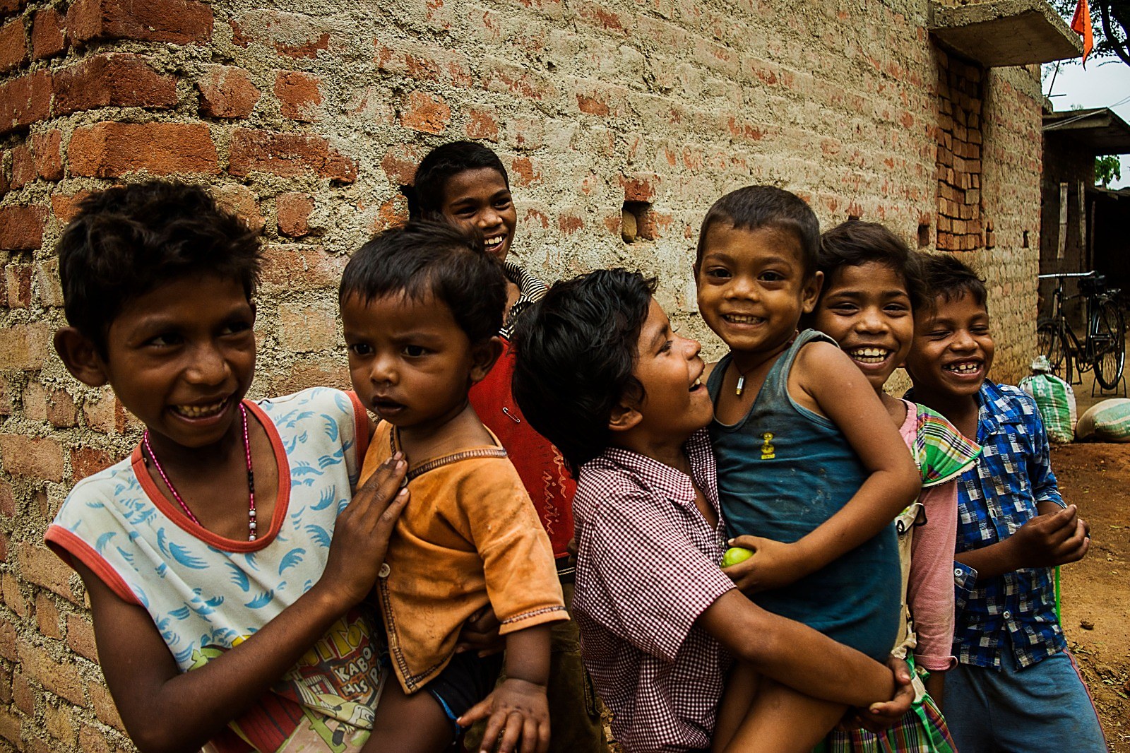 Village children laughing together beside a brick wall
