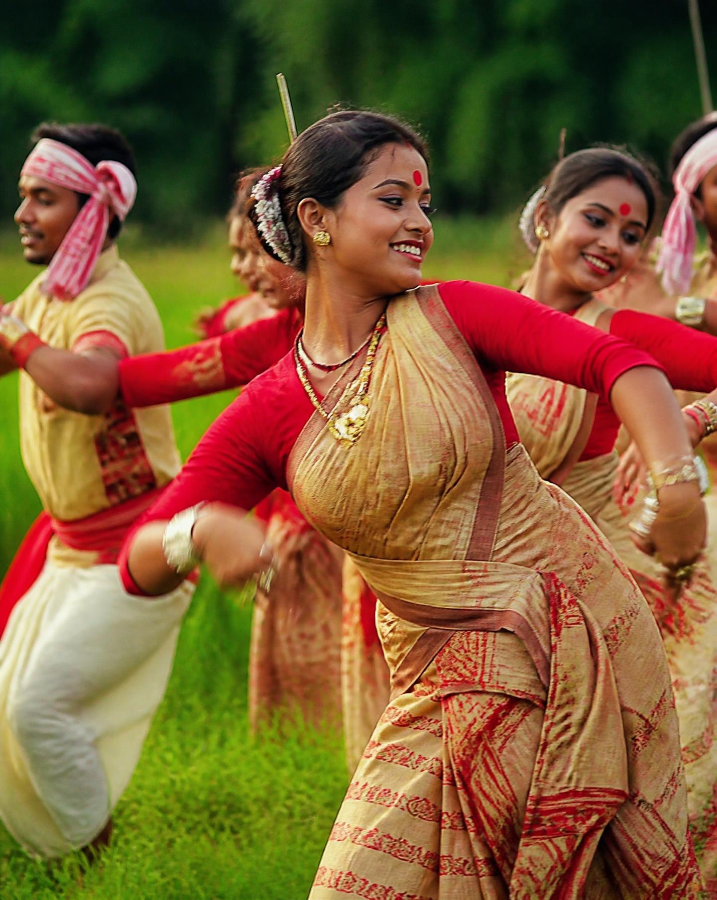 Bihu dancers mid-motion in a green paddy field